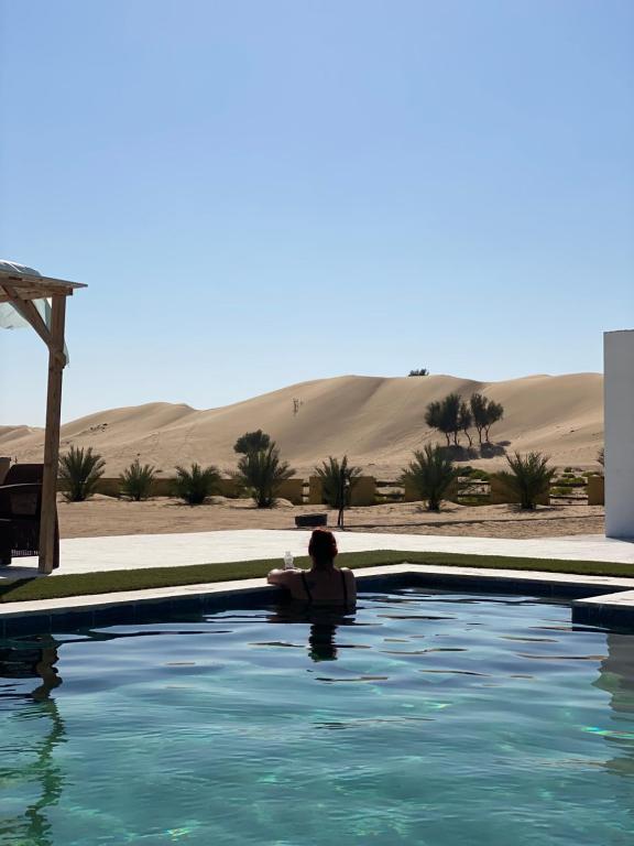 une personne assise dans une piscine dans le désert dans l'établissement Golden Palm Oasis, à Fulayj al Mashāʼikh