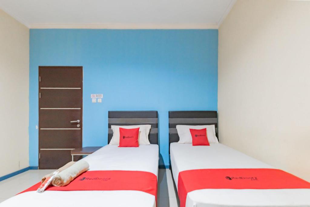 2 łóżka w pokoju z niebieskimi ścianami i czerwonymi poduszkami w obiekcie RedDoorz Syariah @ Pangeran Suryanata Samarinda w mieście Samarinda