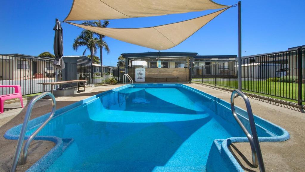 a blue swimming pool with a large umbrella at Ocean Bridge Lakes Entrance in Lakes Entrance
