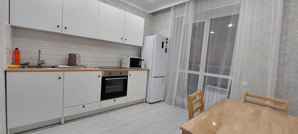 uma cozinha com armários brancos, uma mesa e um frigorífico em Аэропорт 10 минут жк Будапешт163 em Astana