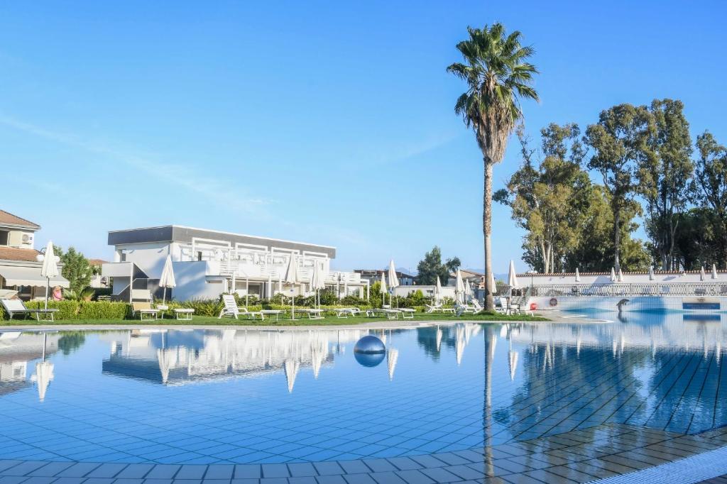 una piscina con una palmera y un edificio en Salice Resort en Marina di Schiavonea