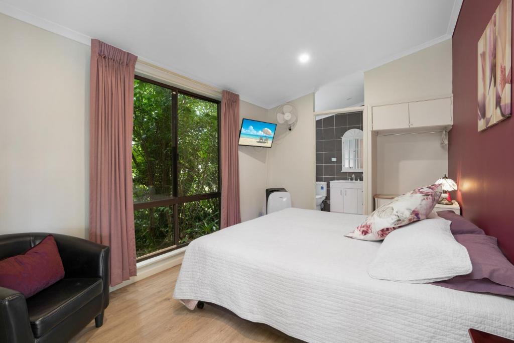 a bedroom with a bed and a chair and a window at Laurelview Scenic Inn Gympie in Gympie