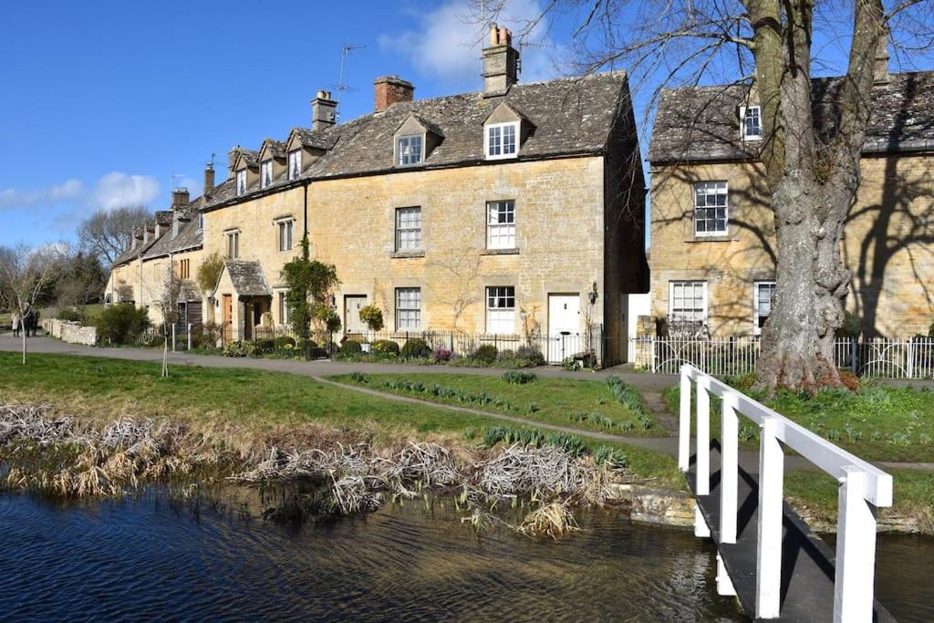 a large brick building next to a river with a bridge at Riverside Cottage in Lower Slaughter