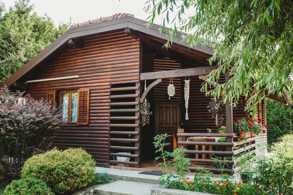 una cabaña de madera con porche y flores frente a ella en River fantasy ( Mrežnička fantazija ) en Duga Resa