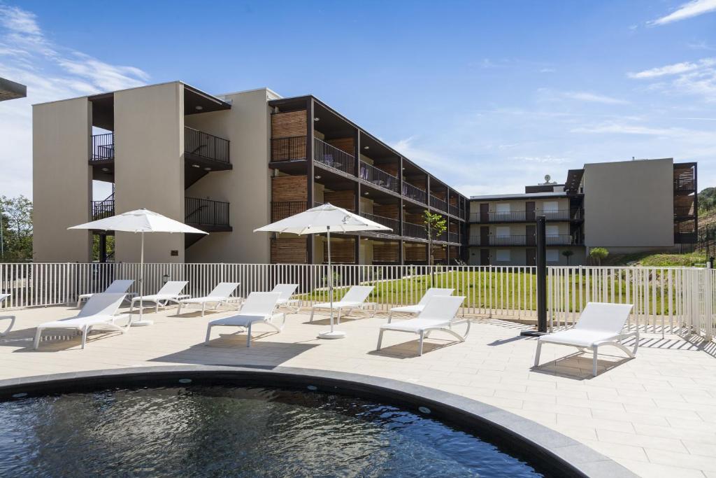 a pool with chairs and umbrellas in front of a building at Vacancéole - Résidence Pont du Gard in Remoulins