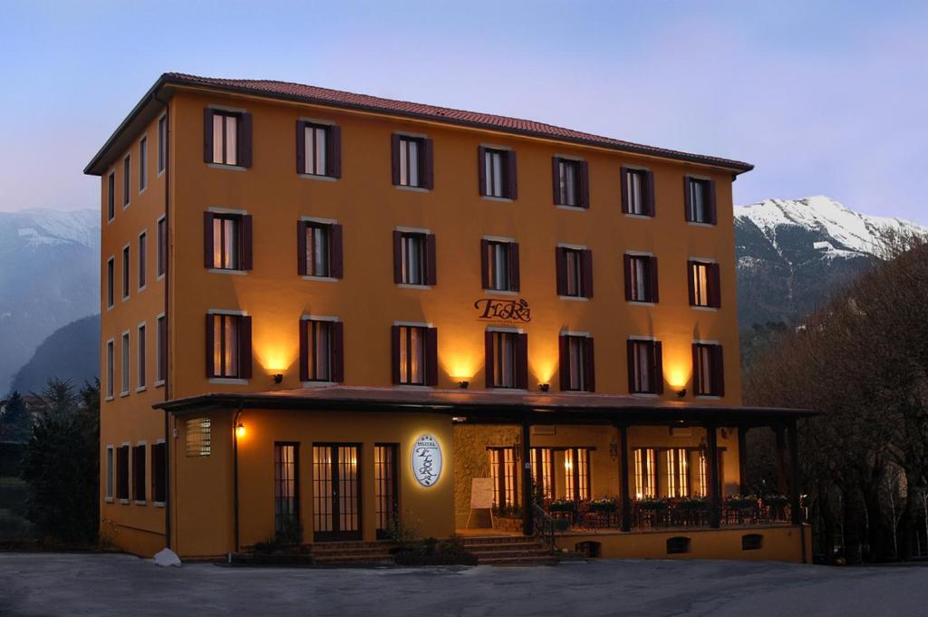 a large yellow building with a snow covered mountain at Albergo Ristorante Flora in Vittorio Veneto