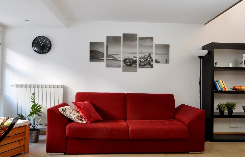 a red couch in a living room with a clock on the wall at Loft ristrutturato vicino M4 Argonne - San Benigno in Milan