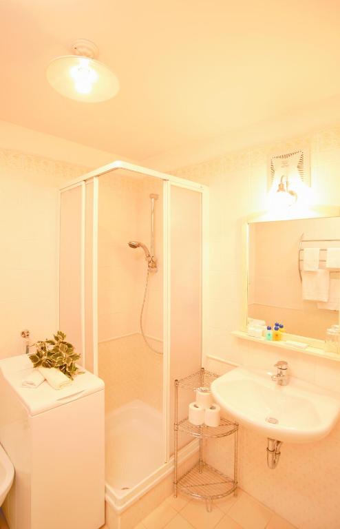 biała łazienka z prysznicem i umywalką w obiekcie Hotel Tschurtschenthaler w mieście Dobbiaco