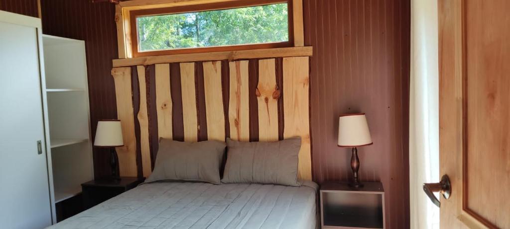 1 dormitorio con 1 cama con cabecero de madera y ventana en Huallerupe Lodge, en Melipeuco