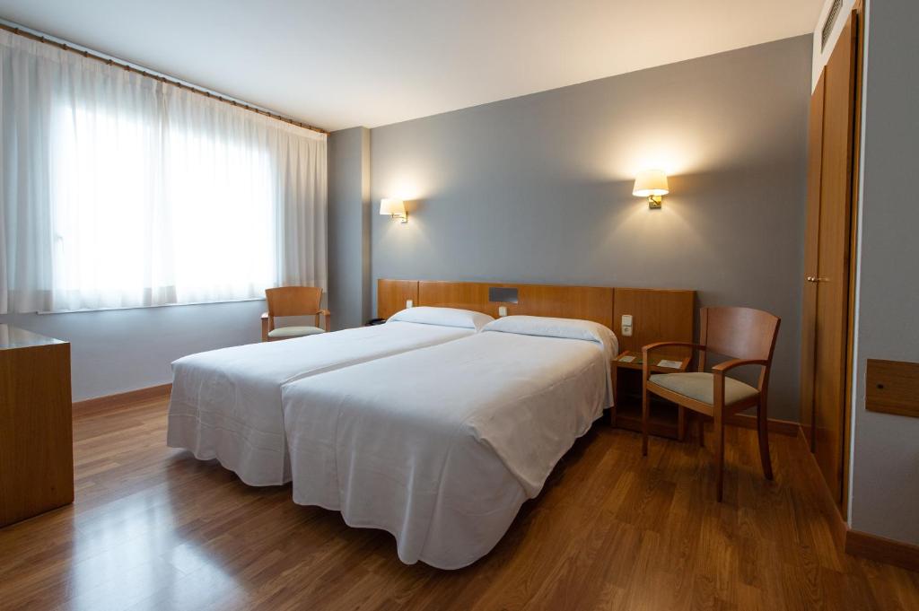 a bedroom with a large white bed and a desk at Hotel Borrell in Olot