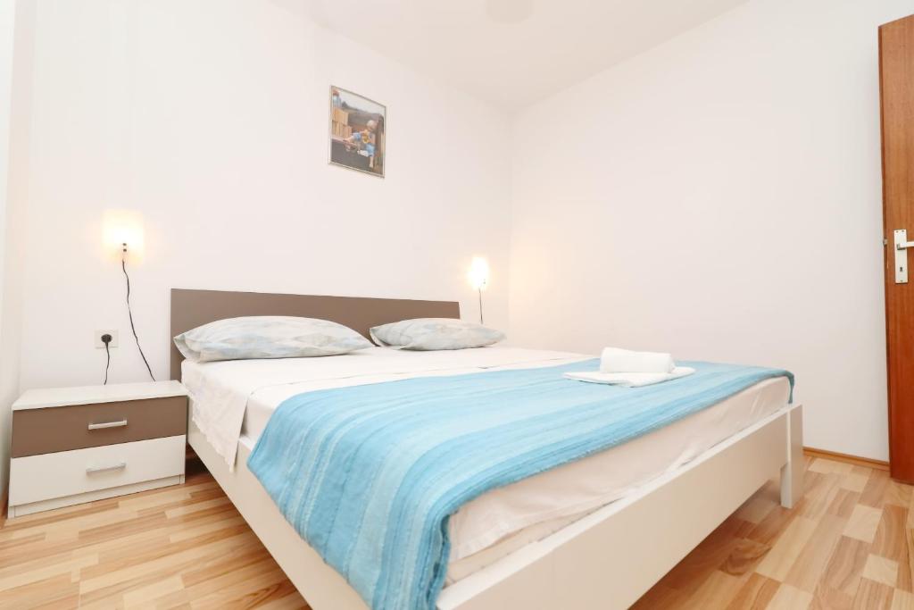 biała sypialnia z łóżkiem z niebieskim kocem w obiekcie Apartments Prižba Bay w mieście Prižba