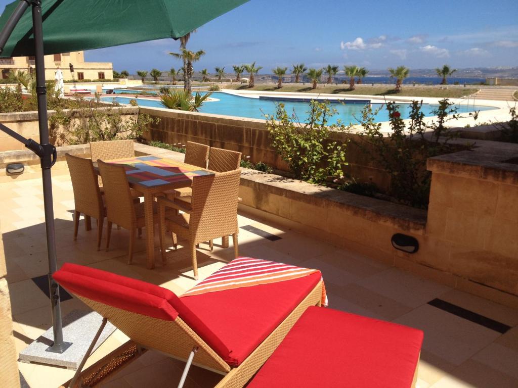 een patio met een tafel en stoelen en een zwembad bij Fort Chambray Apartment in Għajnsielem