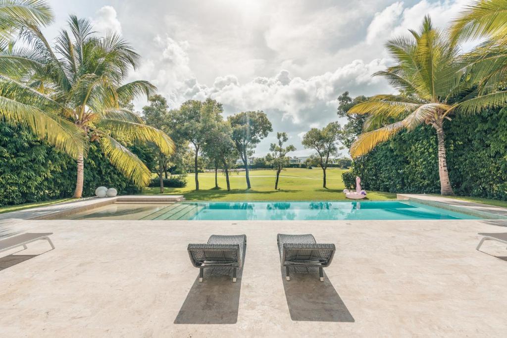 a swimming pool with two chairs and palm trees at Majestic Golf View 4BR Villa at Punta Cana Resort in Punta Cana