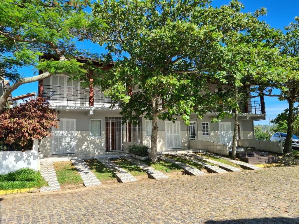 une maison blanche avec un arbre en face dans l'établissement RESIDENCIAL COM CASAS DE 3 DORM, à Garopaba