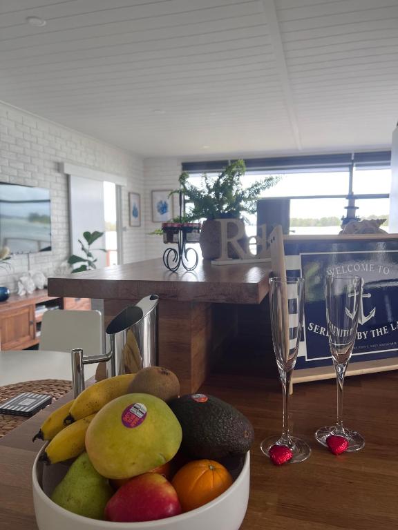 a bowl of fruit on a table with wine glasses at Serenity by the Lake - Romantic Waterfront Couple's Getaway in Marks Point