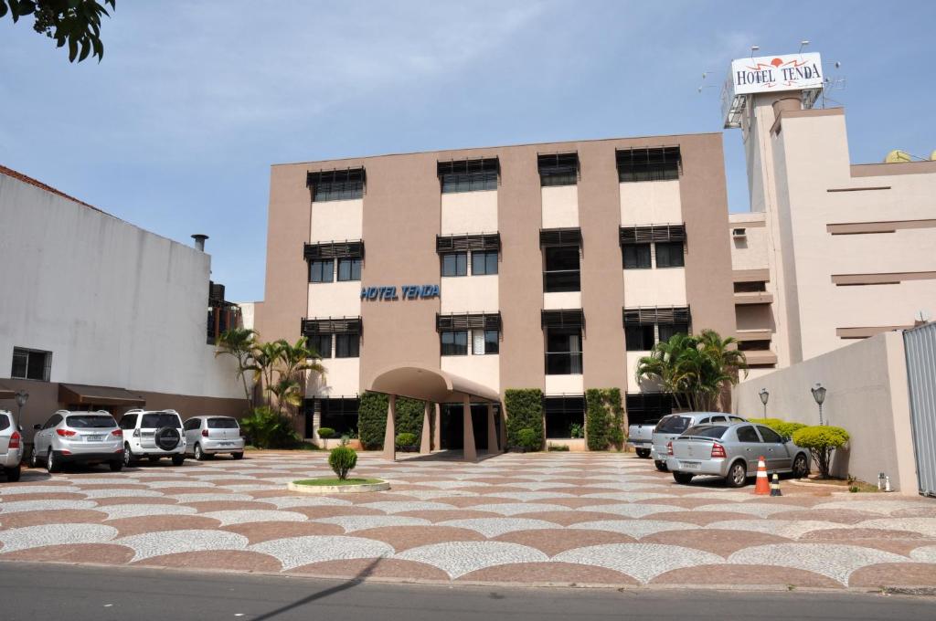 een groot gebouw met auto's geparkeerd op een parkeerplaats bij Hotel Tenda in Marília