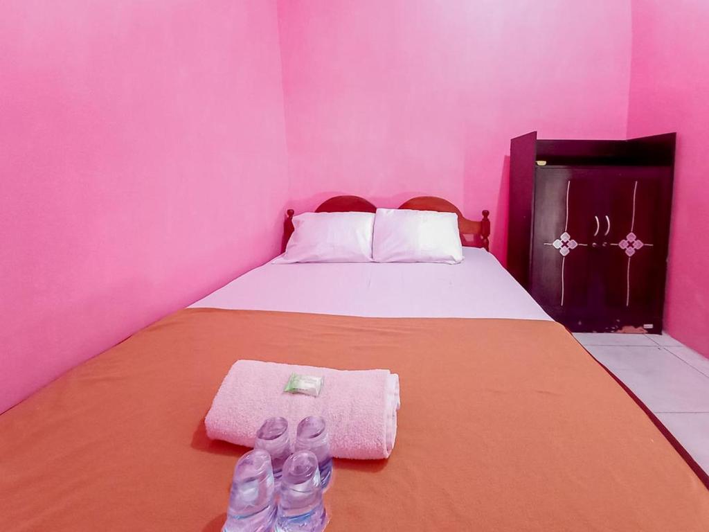 a pink bedroom with a bed with a pair of slippers at Papilo House near Stasiun Nganjuk Mitra RedDoorz in Nganjuk