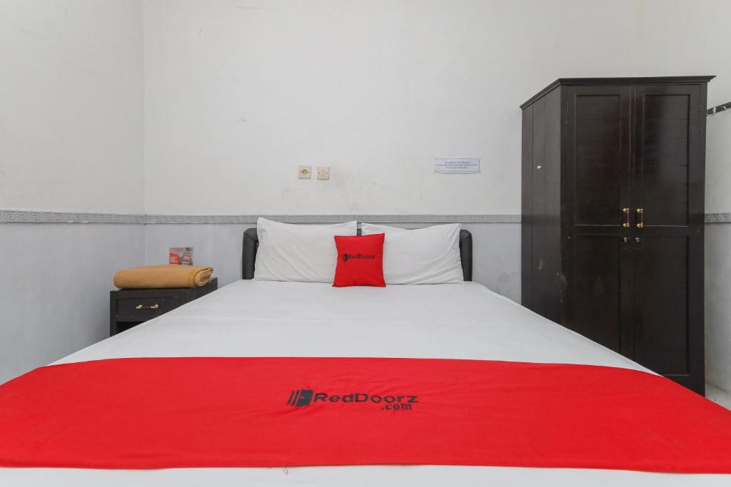 Una cama con una almohada roja encima. en RedDoorz near Stasiun Malang Kota Lama 2, en Malang
