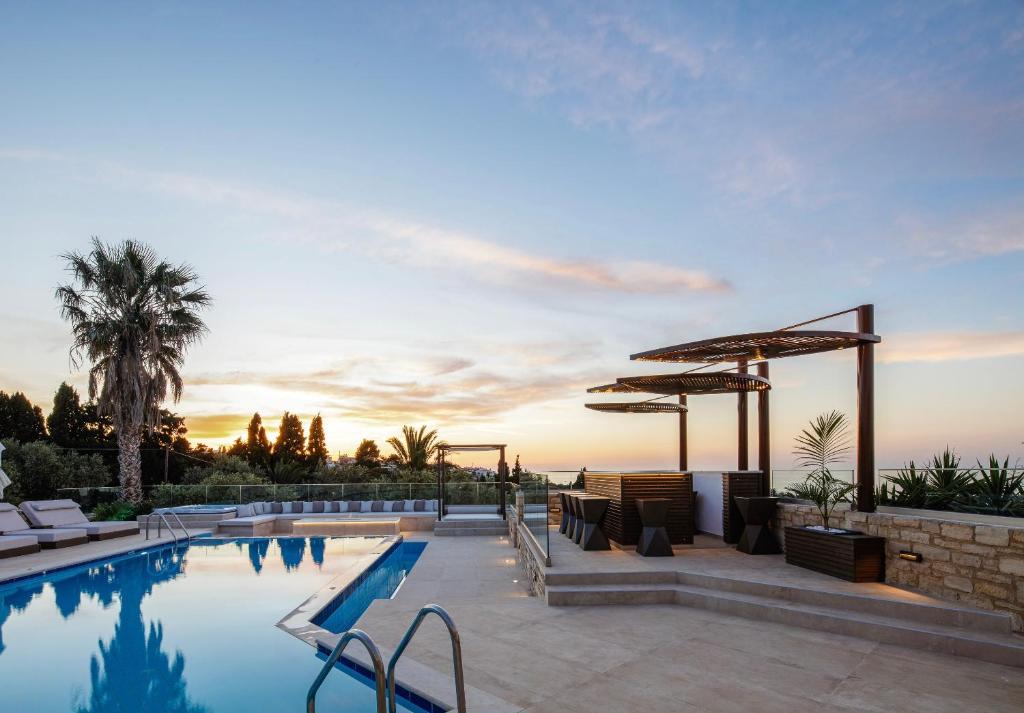 a pool with chairs and umbrellas at sunset at Alpha Luxury & Spa Villa in Rethymno Town