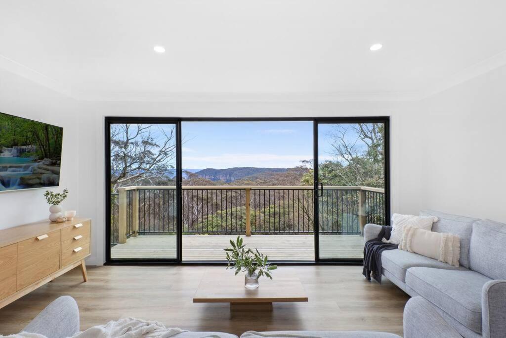 Una sala de estar con un sofá y puertas corredizas de vidrio. en Megalong Valley Lookout Cottage, en Katoomba