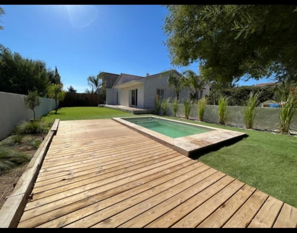 un patio trasero con terraza de madera y piscina en Villa Junna en Fréjus