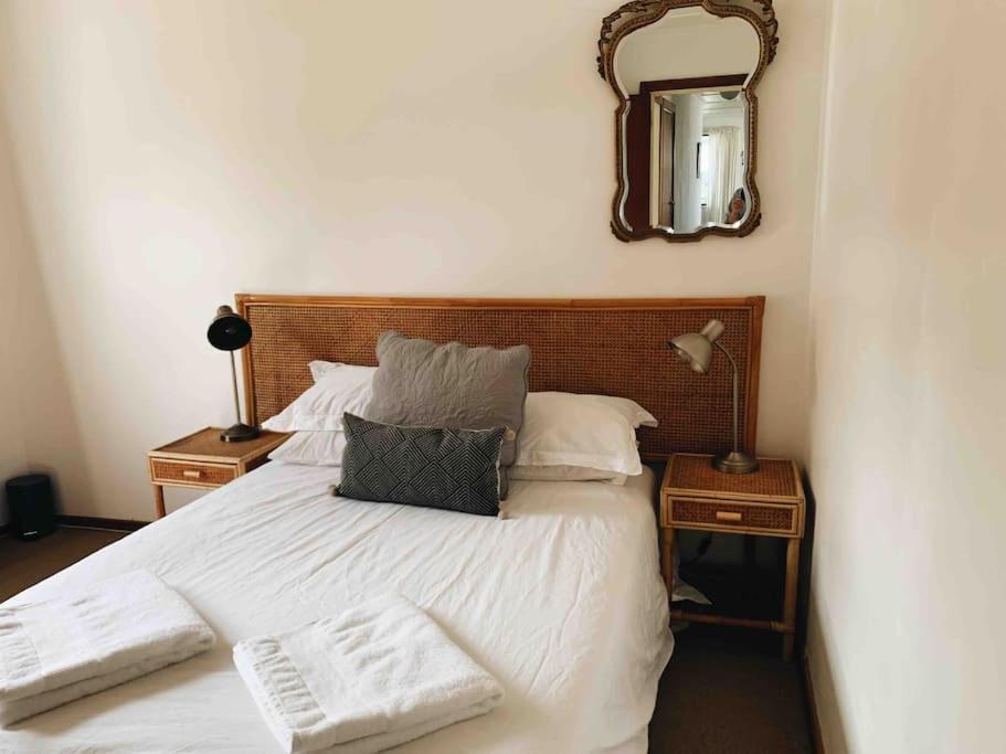 a bedroom with a white bed with a mirror on the wall at Sweet & Simple Beach Cottage in Jeffreys Bay