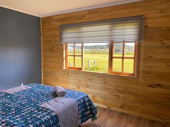 Schlafzimmer mit einem Bett und einem Fenster mit einem Feld in der Unterkunft Cabañas del Llano in Puyehue