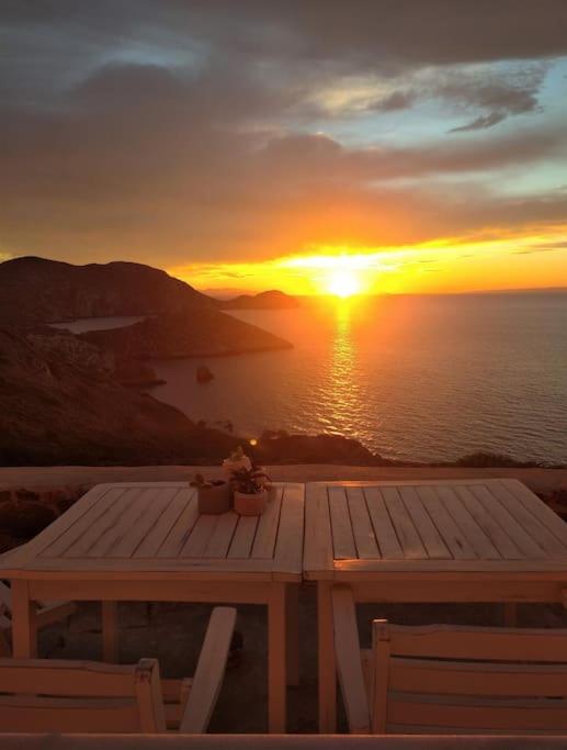 a sunset over the ocean with a wooden table and chairs at C & C _ Cycladic house with endless sea view in Ermoupoli