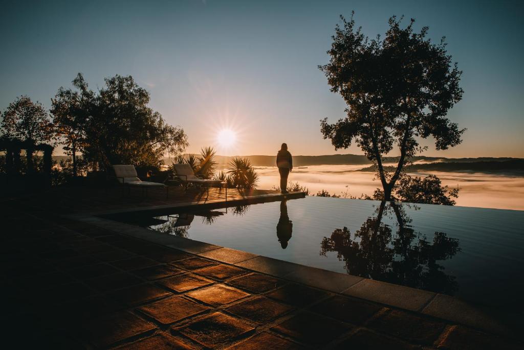 una persona de pie junto a una piscina con puesta de sol en TheVagar Countryhouse, en Belmonte