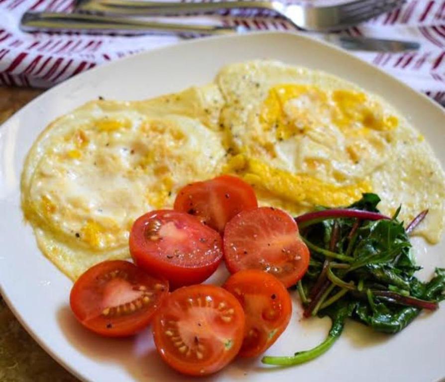 a plate of food with eggs and tomatoes and greens at Riru girlstay in Patna