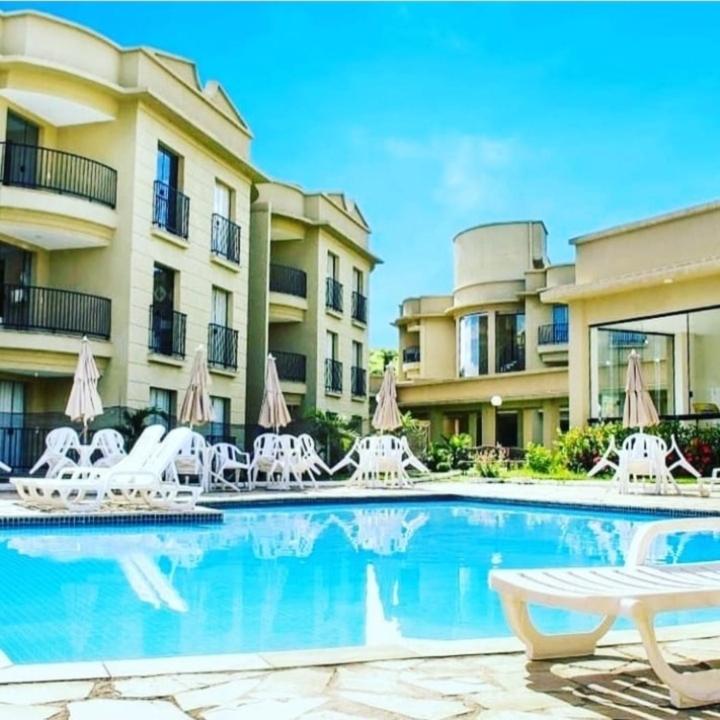 a swimming pool with white chairs and a building at Flat_Quartie_aldeia_das_aguas in Barra do Piraí