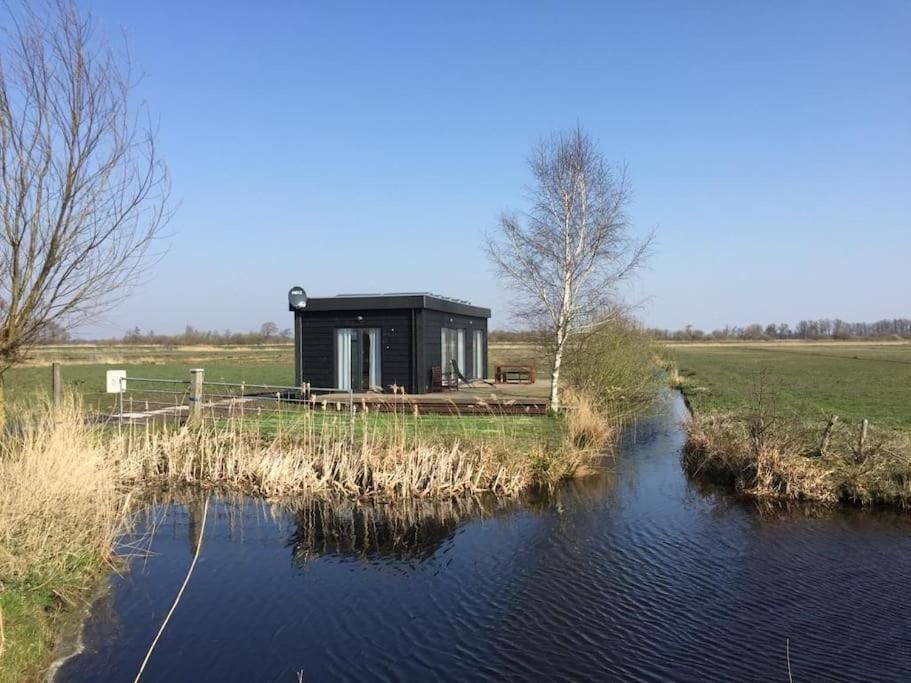 a black house sitting on the side of a river at De Veenweide in De Veenhoop