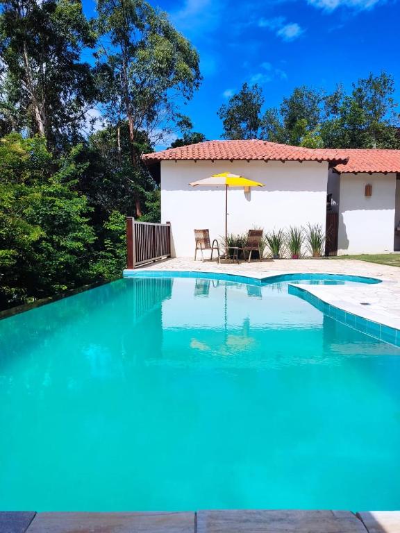 a pool with an umbrella and a house at Pousada Aroeira in Itaúnas