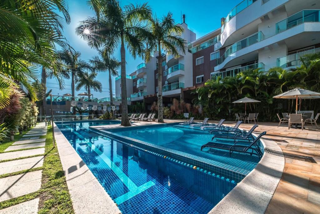 a swimming pool with chairs and palm trees in front of a building at Boulevard 221D - Excelente apartamento em condomínio de luxo no centro de Bombinhas - Piscina - Jacuzzi - Academia - Portaria 24h - (Consultar serviços de roupa de cama e banho) in Bombinhas