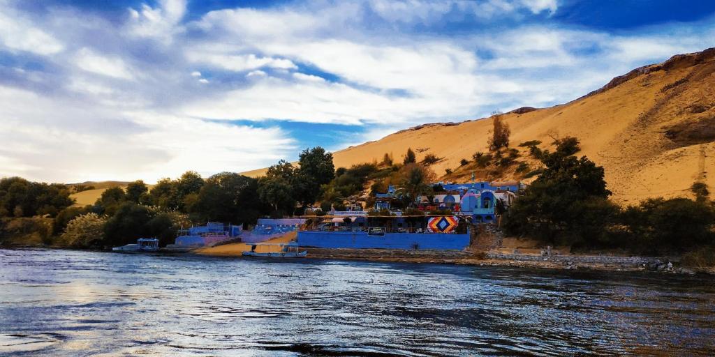 a blue boat on a river next to a mountain at Nubian Beach - حسن فوكس in Aswan