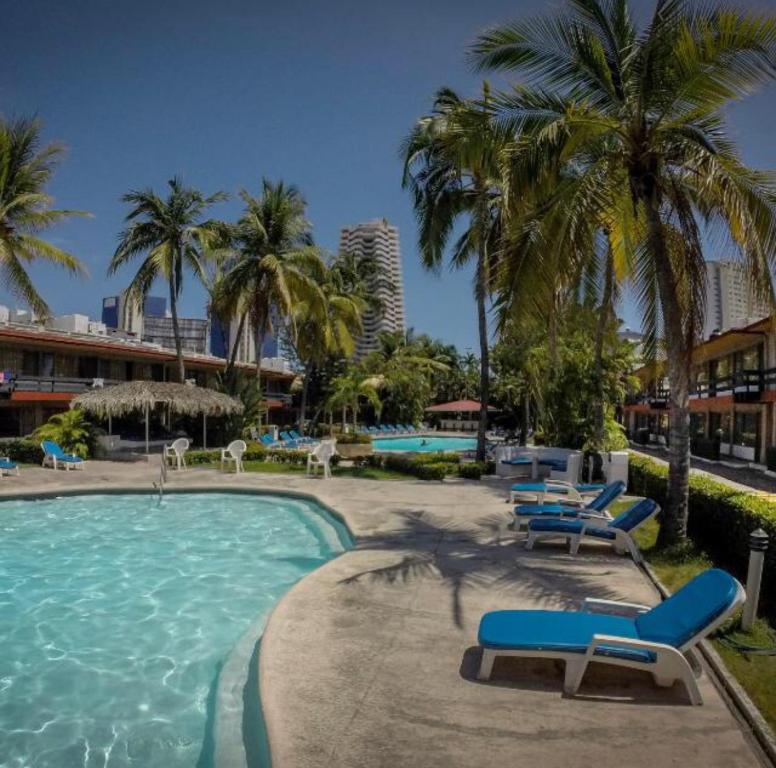 una piscina con sillas y palmeras en un complejo en Hotel Bali-Hai Acapulco, en Acapulco