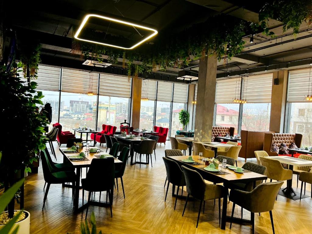 uma sala de jantar com mesas, cadeiras e janelas em Graf Hotel em Shymkent