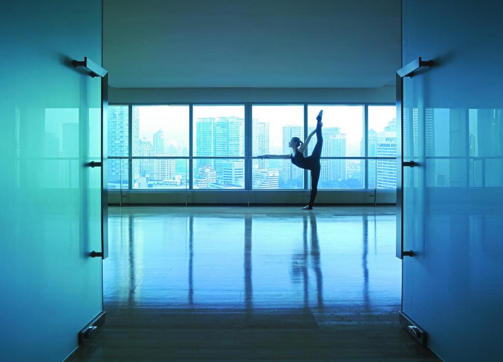 A bright fitness studio opens onto a skyline view through a full wall of windows.