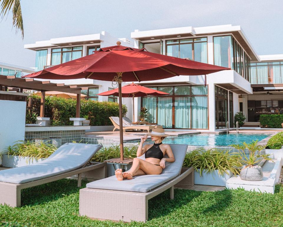 Tolani Le Bayburi Villas, Hua Hin - Pranburi في بران بوري: امرأة جالسة على كرسي بجوار حمام السباحة