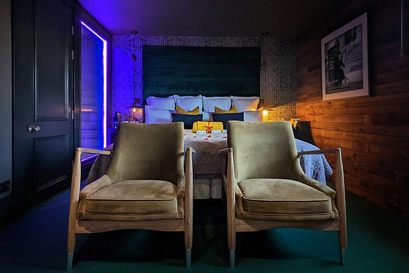 a bedroom with two chairs and a bed with a purple light at The Bells - Luxury Serviced Apartments in Leeds