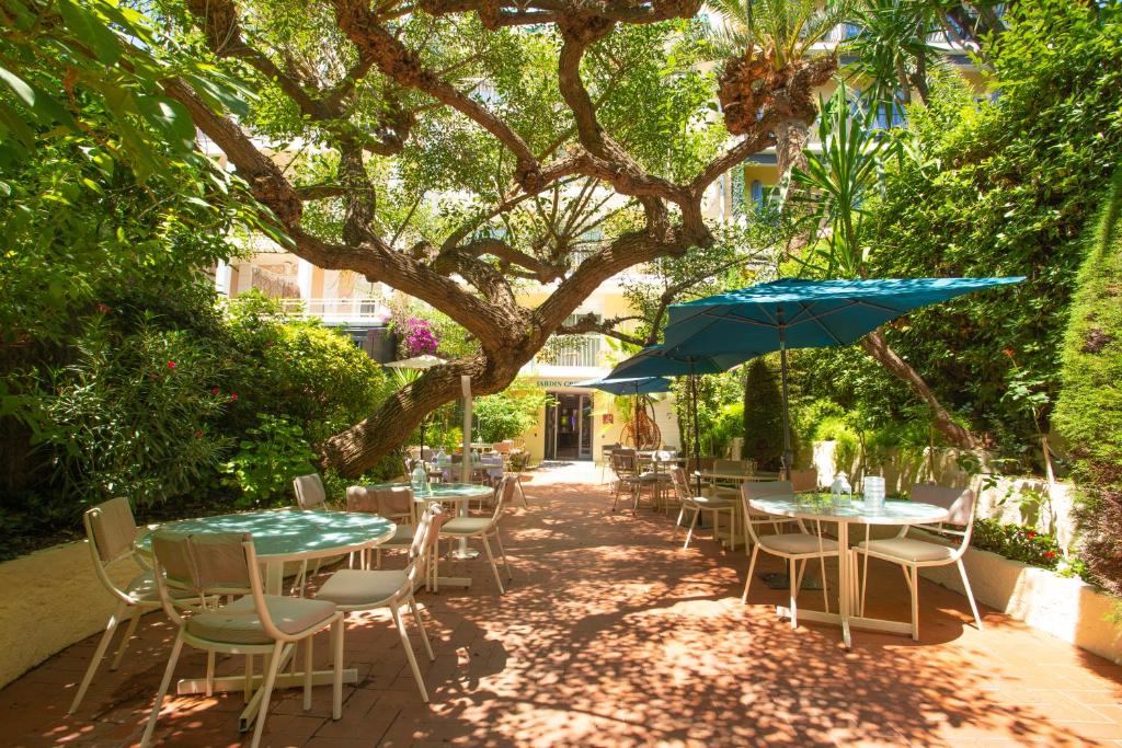 a patio with tables and chairs and an umbrella at Hôtel Jardin Croisette in Cannes