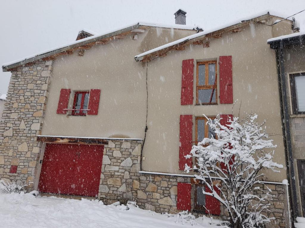 una casa cubierta de nieve con ventanas de contraventanas rojas en Maison de montagne dans charmant village du Capcir, en Fontrabiouse