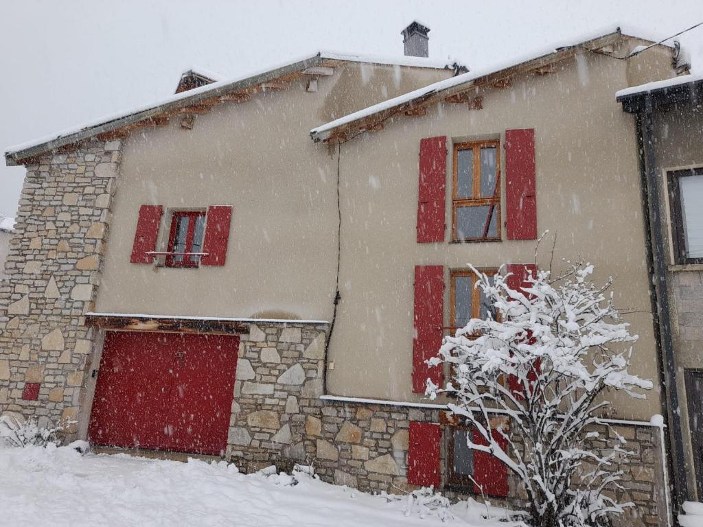 une maison recouverte de neige avec des fenêtres à volets rouges dans l'établissement Maison de montagne dans charmant village du Capcir, à Fontrabiouse