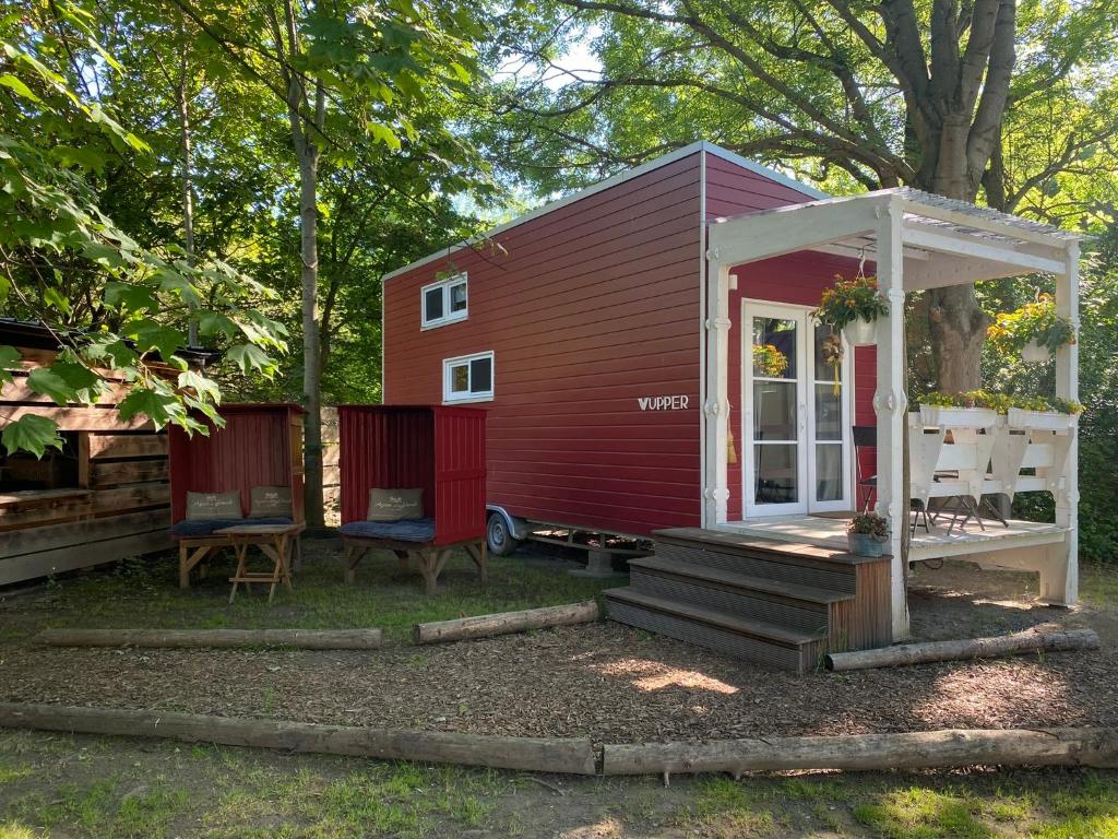 une petite maison rouge avec une porte blanche et une véranda dans l'établissement Tiny House Wupper im PIER9 Tiny House Hotel, à Hamm