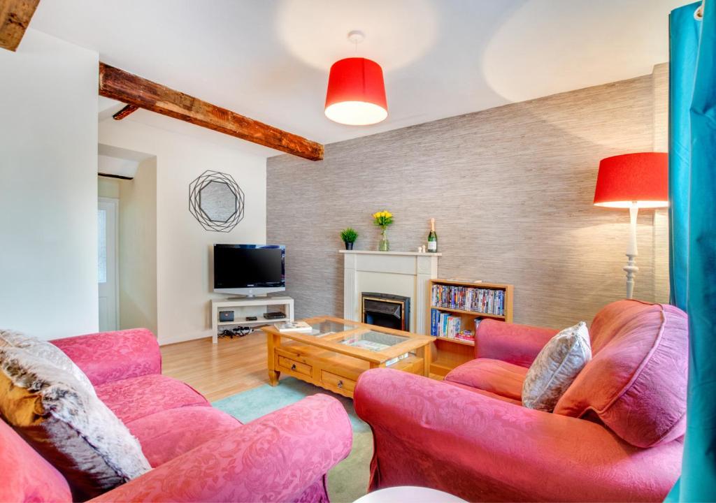 un soggiorno con sedie rosa e TV di Greyhound Cottage a Kendal