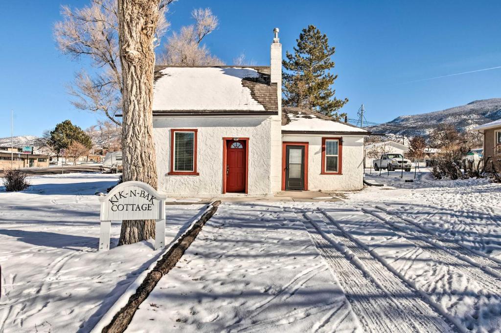 a small white house with a red door in the snow at Kik-N-Bak Cottage with Beautiful Mountain View in Manti