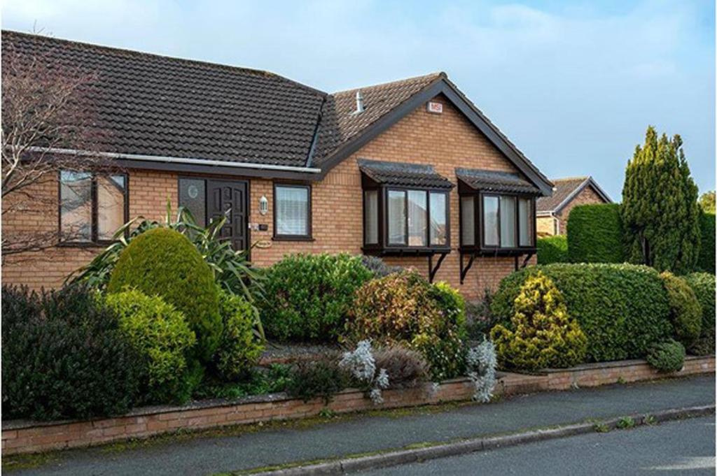 a brown brick house with bushes and trees at Aderyn Du in Abergele