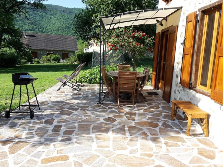 a patio with a table and an umbrella and a grill at Grange en pierres. Grand jardin et belle vue in Saurat