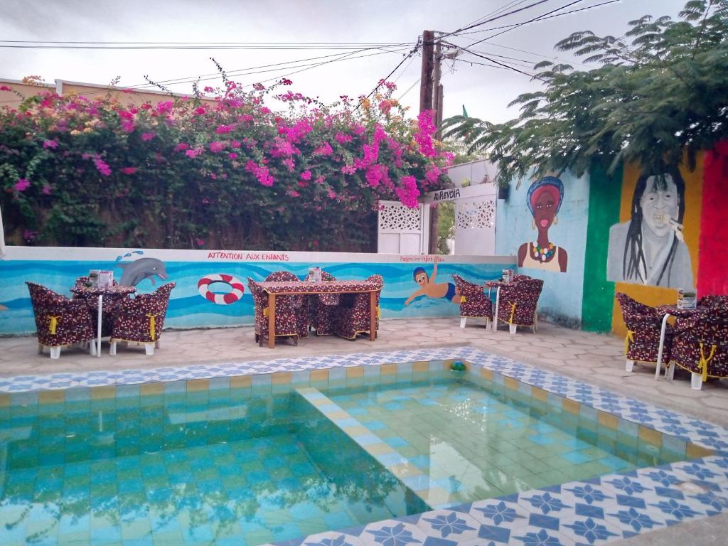 una piscina con mesas y sillas junto a una pared con una pintura en Auberge Africa Thiossane, en Saly Portudal