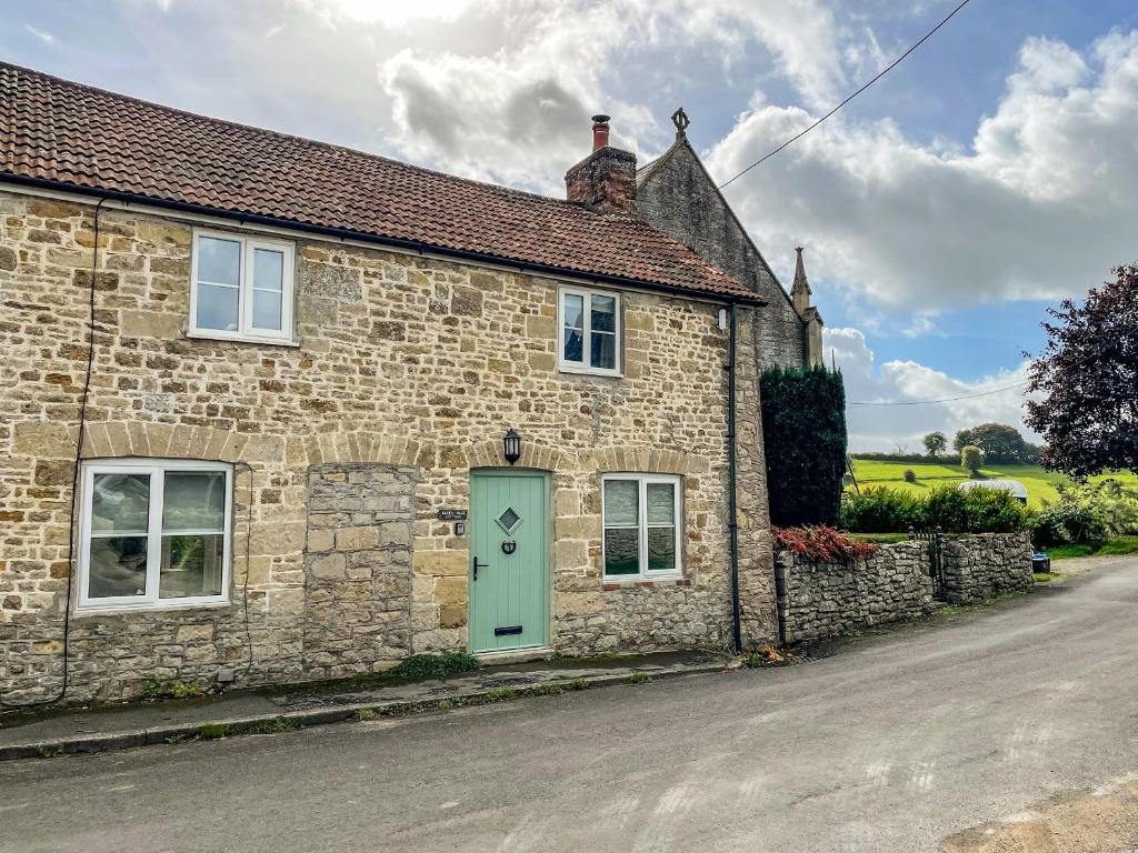 a stone cottage with a green door on a street at Greenhills Cottage in Shepton Mallet